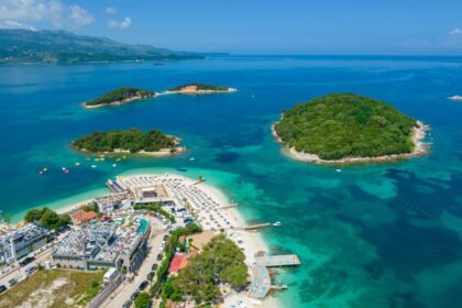 Vue aérienne des îlots verdoyants de Ksamil dans une eau turquoise, avec les rangées de transats alignées sur la plage