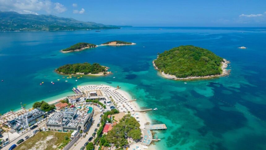 Vue aérienne des îlots verdoyants de Ksamil dans une eau turquoise, avec les rangées de transats alignées sur la plage