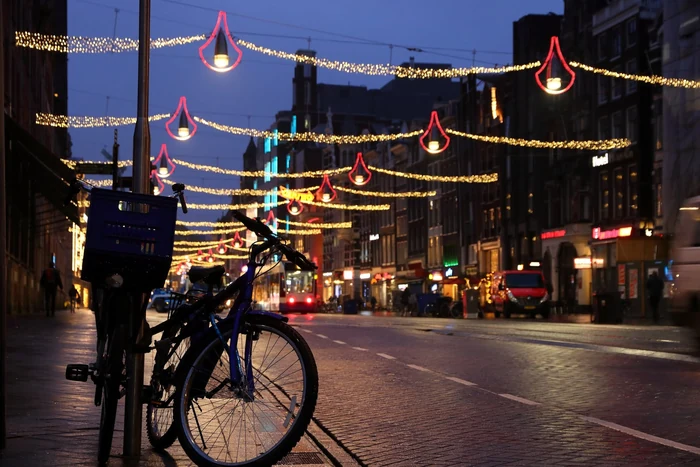 Une rue d'Amsterdam le soir en décembre, traversée de guirlandes lumineuses et bordée de vélos