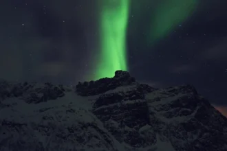 Une aurore boréale verte déployée en rideau au-dessus d'une montagne enneigée près de Tromsø, en Norvège