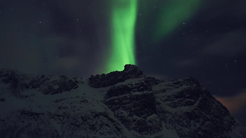 Une aurore boréale verte déployée en rideau au-dessus d'une montagne enneigée près de Tromsø, en Norvège