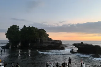 Le temple de Tanah Lot à Bali en silhouette au coucher du soleil, avec les visiteurs massés sur le rivage