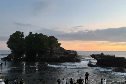 Le temple de Tanah Lot à Bali en silhouette au coucher du soleil, avec les visiteurs massés sur le rivage