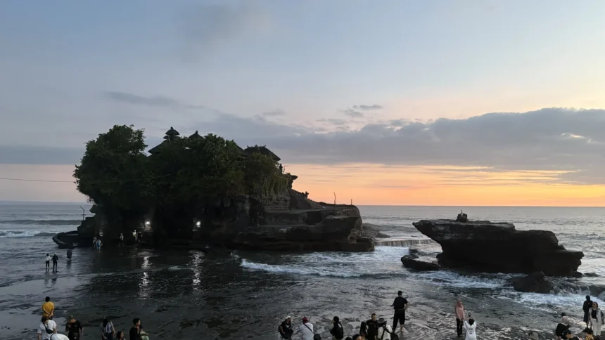Le temple de Tanah Lot à Bali en silhouette au coucher du soleil, avec les visiteurs massés sur le rivage