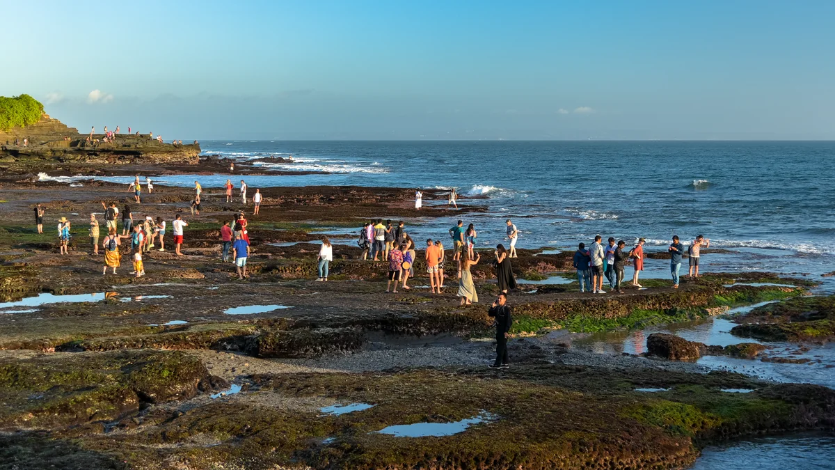 Coucher de soleil à Bali : l'heure exacte mois par mois et les côtes qui le voient vraiment 3 Des visiteurs marchant sur le récif découvert à marée basse au pied du rocher de Tanah Lot