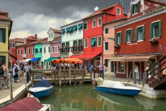 Un canal de Burano bordé de maisons aux façades vivement colorées, avec des barques amarrées et des stores tendus au-dessus des devantures