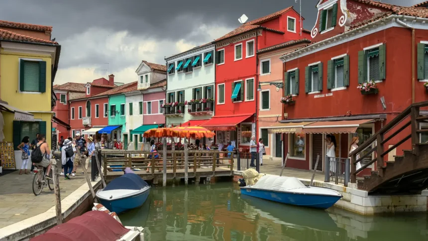 Un canal de Burano bordé de maisons aux façades vivement colorées, avec des barques amarrées et des stores tendus au-dessus des devantures