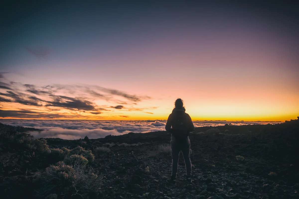 Un coucher de soleil sur un paysage volcanique des Canaries, avec une silhouette de randonneur au premier plan