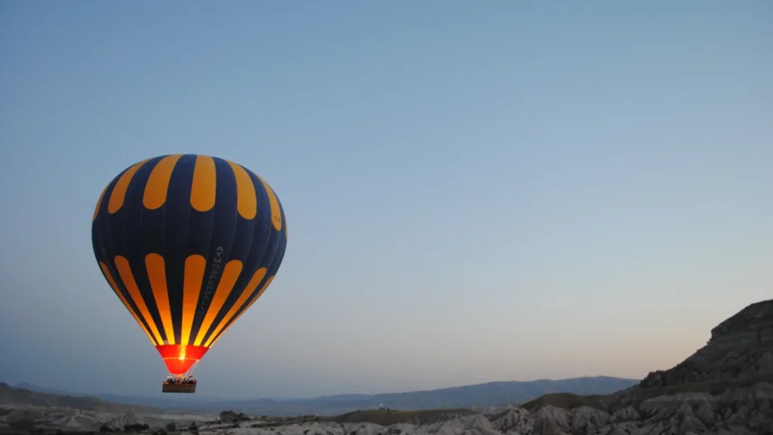 Une montgolfière rayée s'élevant au-dessus des reliefs de Cappadoce au lever du soleil