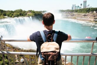 Visiteur accoudé à la rambarde d'un belvédère face aux chutes américaines du Niagara, avec les tours de Niagara Falls en arrière-plan