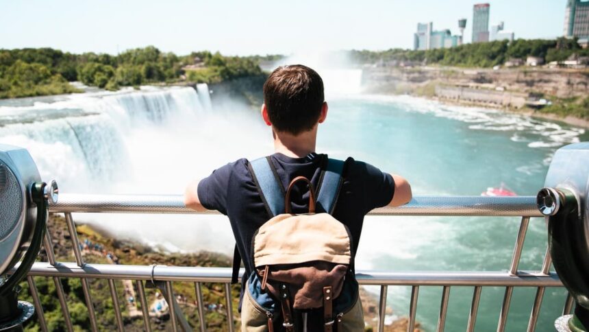 Visiteur accoudé à la rambarde d'un belvédère face aux chutes américaines du Niagara, avec les tours de Niagara Falls en arrière-plan