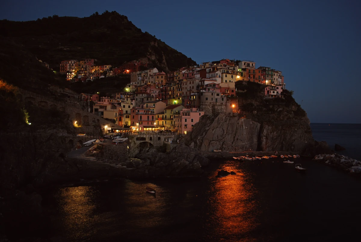 Manarola à la nuit tombée, ses maisons illuminées empilées au-dessus de la mer et leurs reflets sur l'eau
