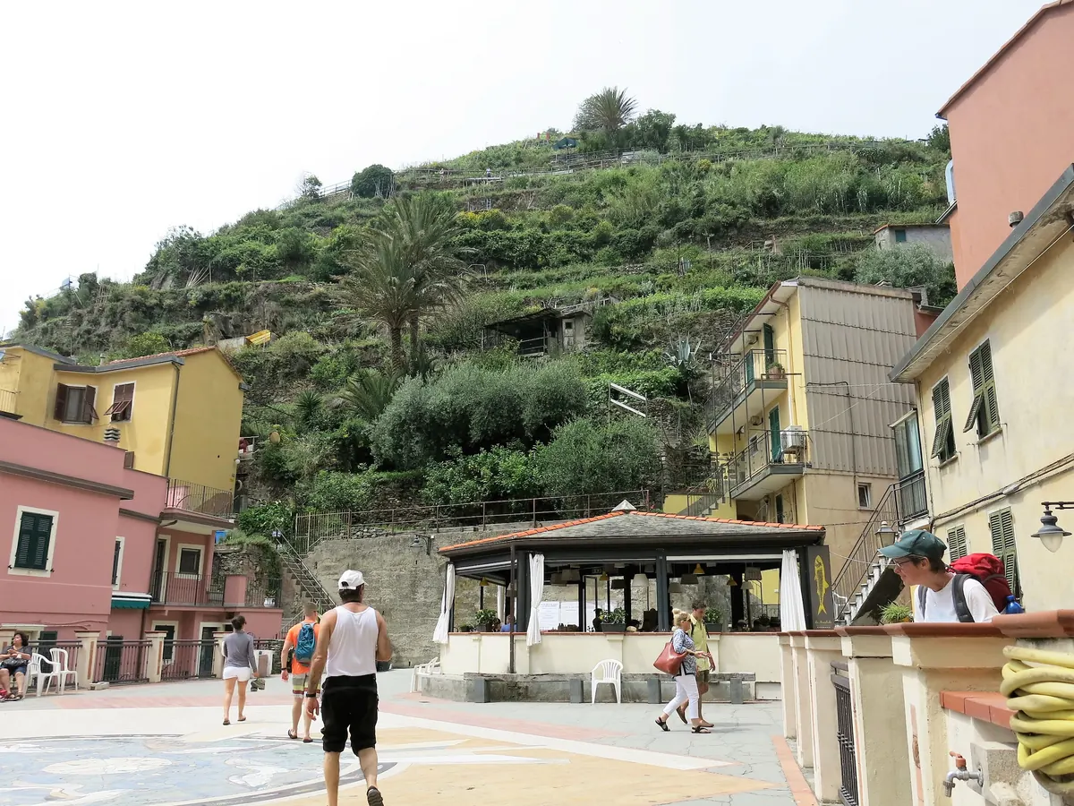 La rue principale d'un village des Cinque Terre, ses façades pastel et ses passants sous les collines en terrasses