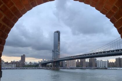 Le pont de Manhattan encadré par une arche de brique depuis les quais de Dumbo à Brooklyn, avec l'East River au premier plan