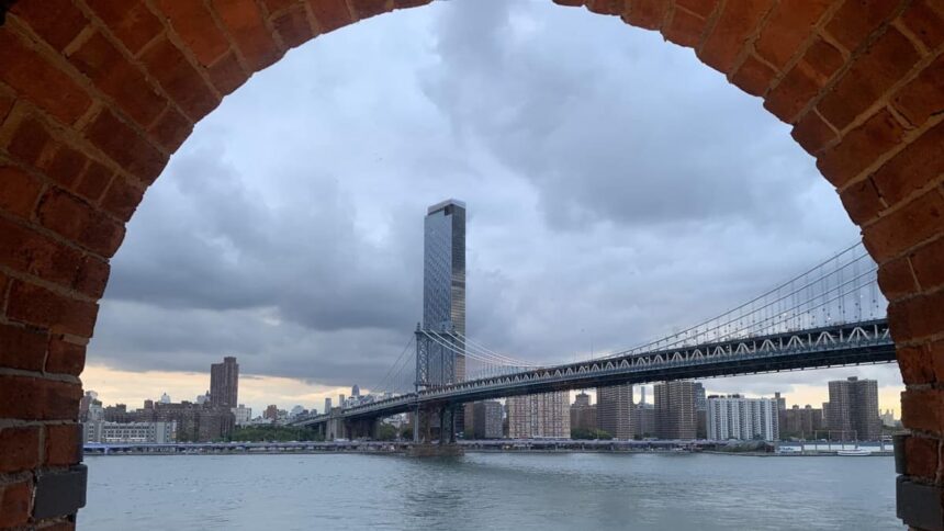 Le pont de Manhattan encadré par une arche de brique depuis les quais de Dumbo à Brooklyn, avec l'East River au premier plan