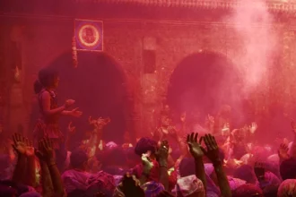Une foule couverte de poudres colorées lors de la fête de Holi en Inde, bras levés dans un nuage rose