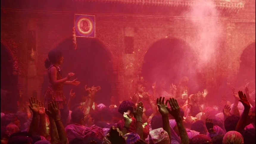 Une foule couverte de poudres colorées lors de la fête de Holi en Inde, bras levés dans un nuage rose