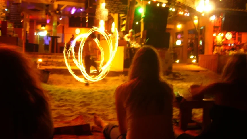Un spectacle de feu devant un bar de plage de Koh Phangan la nuit, avec les silhouettes des spectateurs