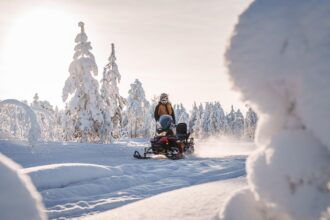 Motoneige sur une piste enneigée entre des arbres givrés, éclairée par le soleil bas de Laponie