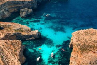 Vue aérienne d'un lagon turquoise entre les rochers calcaires de Comino, à Malte, avec un bateau au mouillage