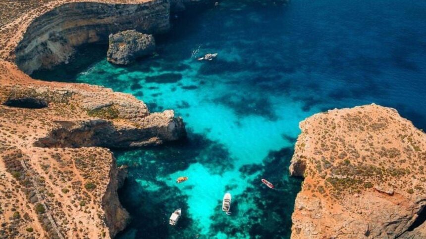 Vue aérienne d'un lagon turquoise entre les rochers calcaires de Comino, à Malte, avec un bateau au mouillage