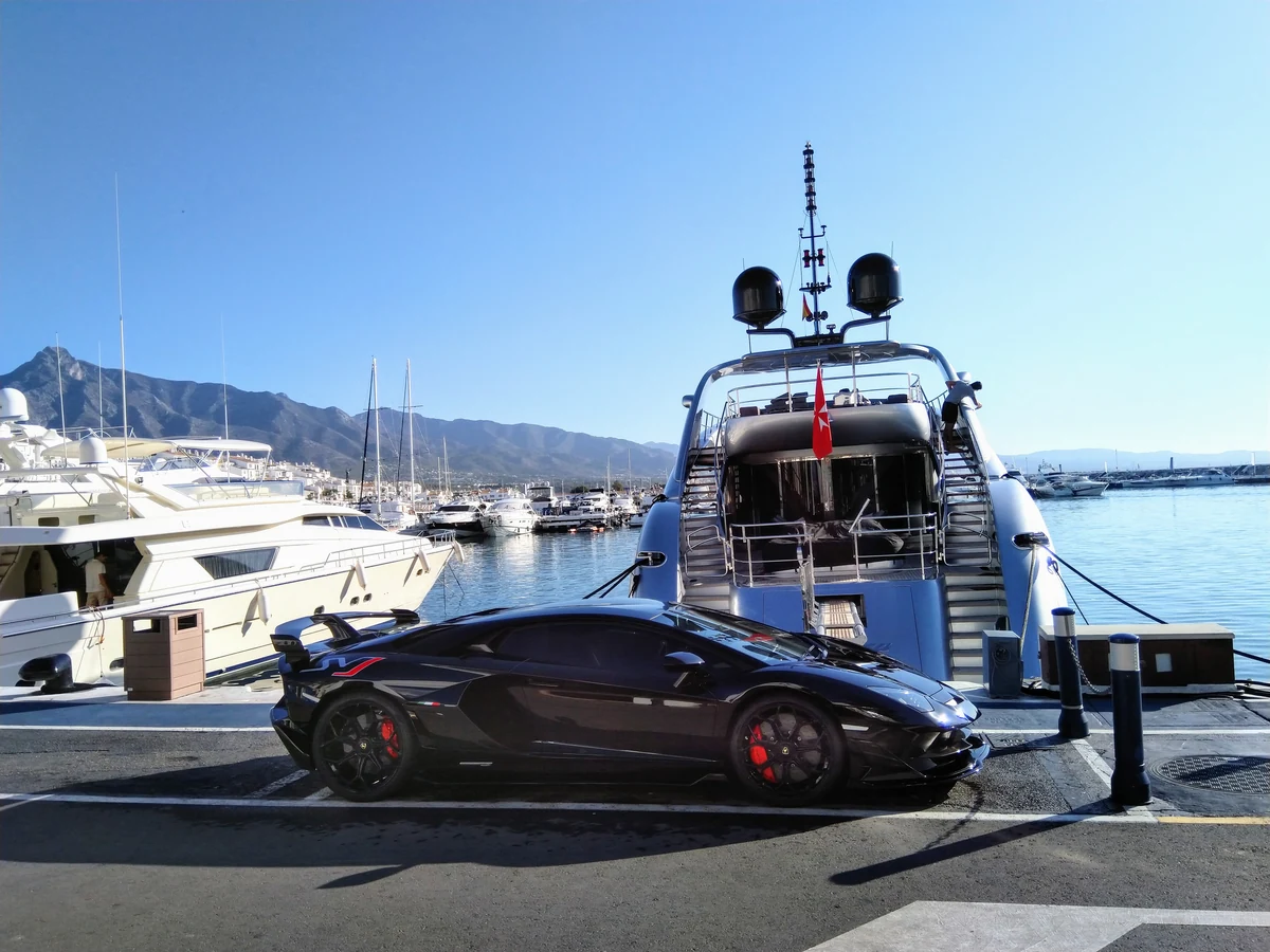 Beach clubs de Marbella : les 10 adresses et le piège du transat qu'on croit payant 3 Un yacht amarré à Puerto Banús et une voiture de sport garée sur le quai