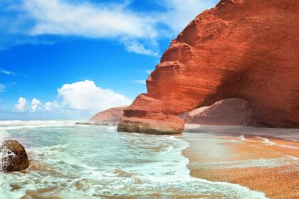 Falaise et arche de grès rouge de Legzira surplombant le sable ocre et l'eau turquoise, sur la côte atlantique marocaine