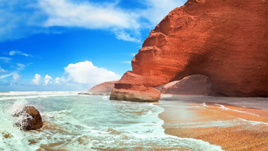 Falaise et arche de grès rouge de Legzira surplombant le sable ocre et l'eau turquoise, sur la côte atlantique marocaine