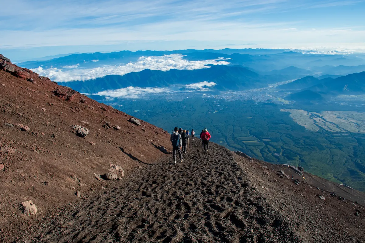 Mont Fuji : le voir et le gravir, deux projets à ne pas confondre 2 Des randonneurs progressant en file sur le sentier de cendre volcanique du mont Fuji, au-dessus de la mer de nuages