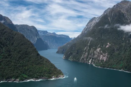 Le fjord de Milford Sound en Nouvelle-Zélande, ses parois boisées plongeant dans l'eau sombre et un bateau minuscule au centre