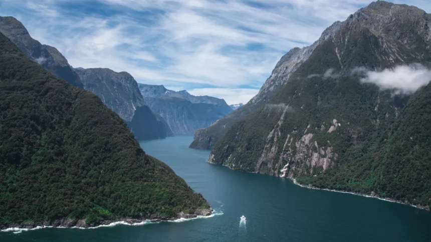 Le fjord de Milford Sound en Nouvelle-Zélande, ses parois boisées plongeant dans l'eau sombre et un bateau minuscule au centre