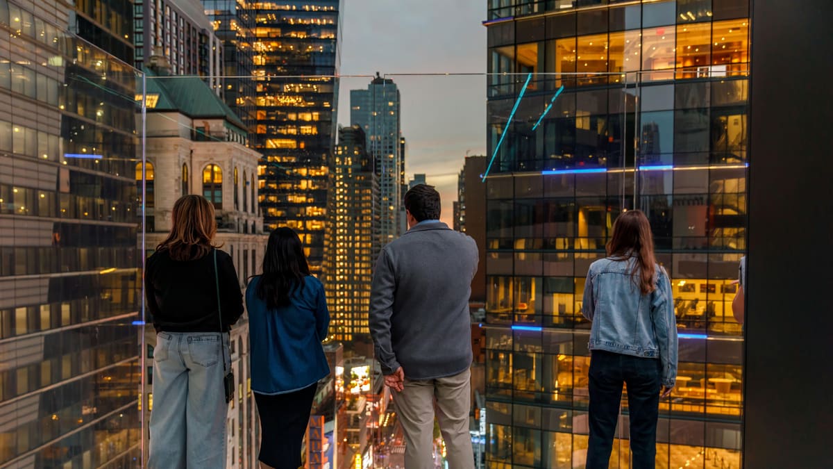 Billets pour le Skywalk One Times Square : prix, horaires et avis du nouvel observatoire 4 Quatre visiteurs de dos sur la terrasse de One Times Square au crépuscule, regardant Times Square illuminé entre deux tours de verre