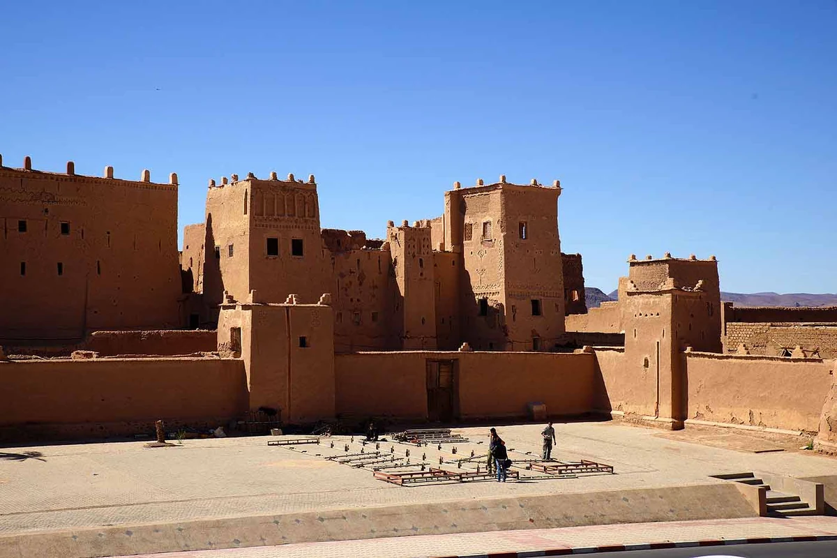 Une kasbah de terre aux hautes tours crénelées près de Ouarzazate, avec sa cour de terre battue et les montagnes arides en arrière-plan