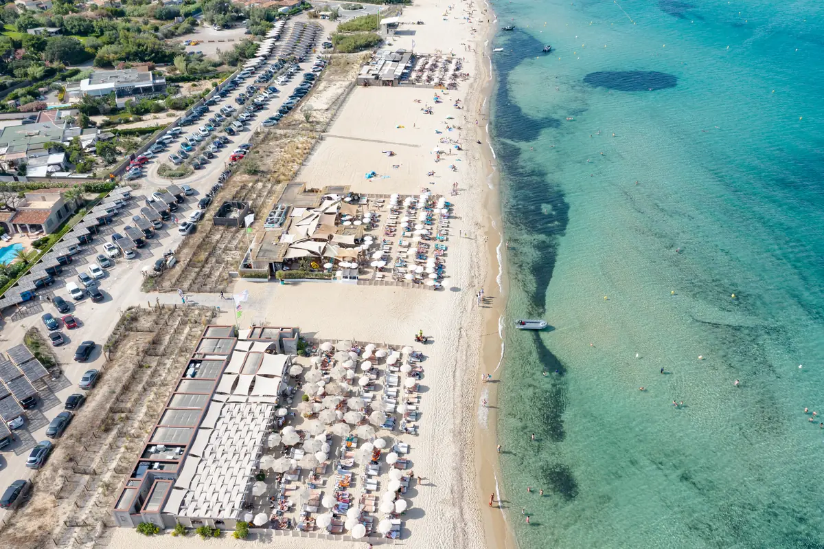 Vue du ciel sur l'alignement des beach clubs de Pampelonne, leurs rangées de parasols, leurs terrasses de restaurant et le parking qui les dessert