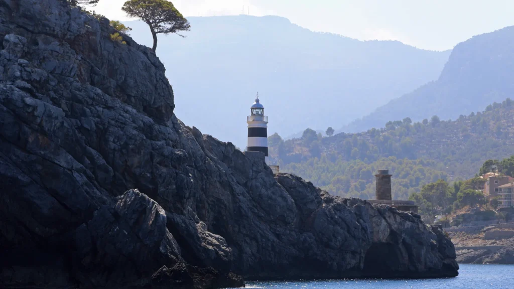 Port de Sóller : que faire, quelle plage choisir et où dormir 2 L'entrée de la baie du Port de Sóller vue depuis la mer, avec le phare posé sur la pointe rocheuse et les reliefs de la Serra de Tramuntana en arrière-plan