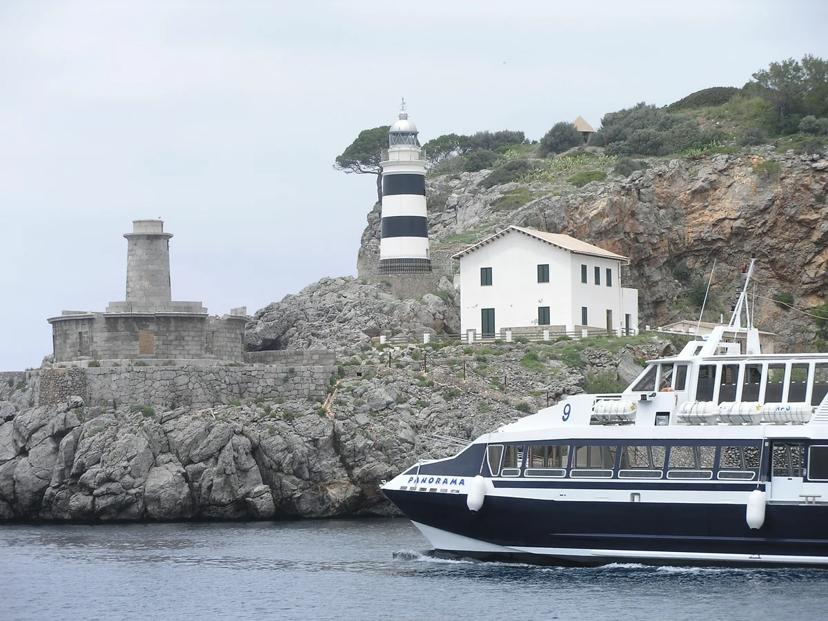 Port de Sóller : que faire, quelle plage choisir et où dormir 5 Un bateau d'excursion quittant le Port de Sóller devant le phare de Sa Creu et les maisons accrochées à la falaise