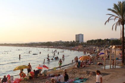 La plage de Salou en fin de journée, avec ses parasols, ses baigneurs et la promenade bordée de palmiers