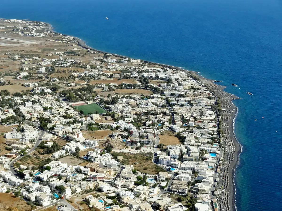 Beach clubs de Santorin : les 8 adresses et la vérité sur Red Beach 3 Vue aérienne d'un village blanc de Santorin accroché à la côte, au-dessus de la mer Égée