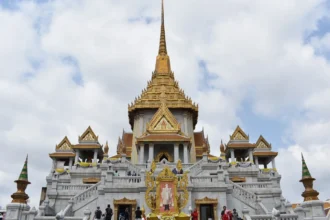 Un temple thaïlandais aux toits dorés étagés, sous un ciel de mousson