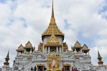 Un temple thaïlandais aux toits dorés étagés, sous un ciel de mousson