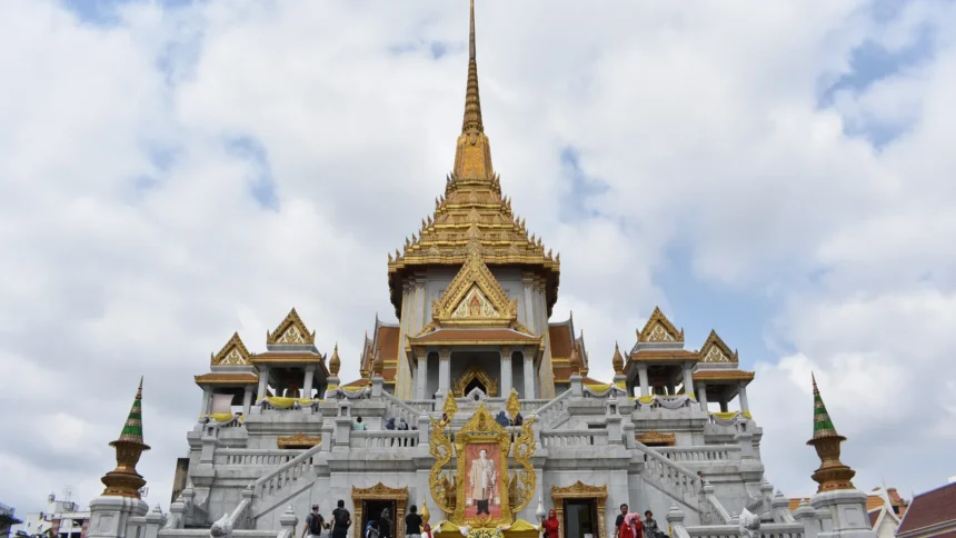 Un temple thaïlandais aux toits dorés étagés, sous un ciel de mousson