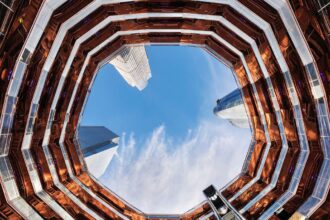 L'intérieur du Vessel à Hudson Yards vu depuis la base, les escaliers de cuivre en nid d'abeille encadrant le ciel et les tours voisines