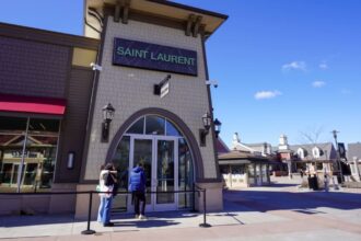 La devanture de la boutique Saint Laurent à Woodbury Common Premium Outlets, deux clientes devant l'entrée et les allées du centre en plein air derrière