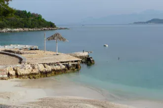 Une plage de Ksamil en Albanie, son ponton de bois avançant sur une eau turquoise et sa bande de sable clair