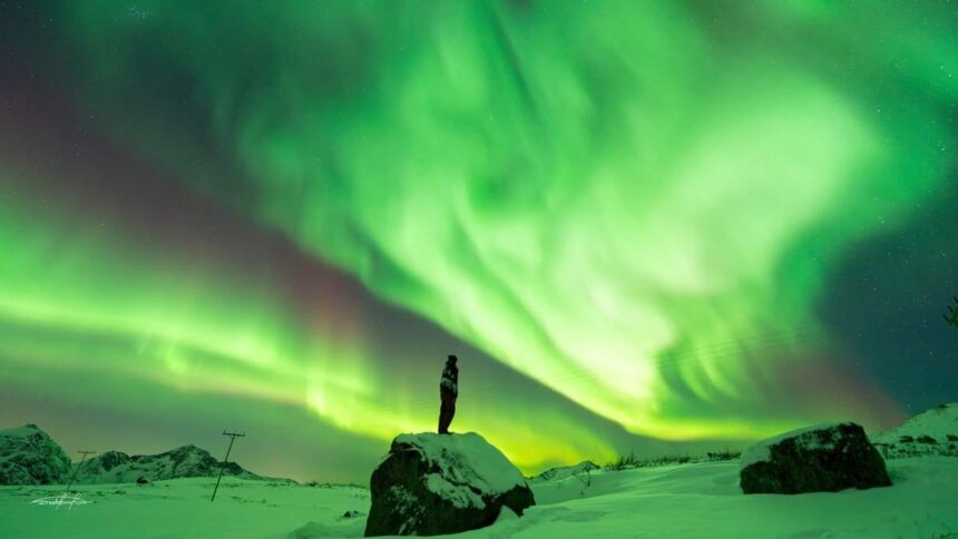 Aurore boréale verte au-dessus d'une plaine enneigée près de Tromsø, en Norvège, avec une personne debout sur un rocher