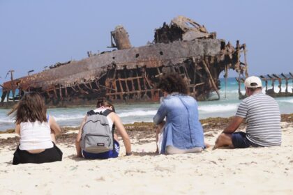 Epave rouillee echouee sur une plage de sable clair de Boa Vista, au Cap-Vert, avec des visiteurs assis face a l ocean