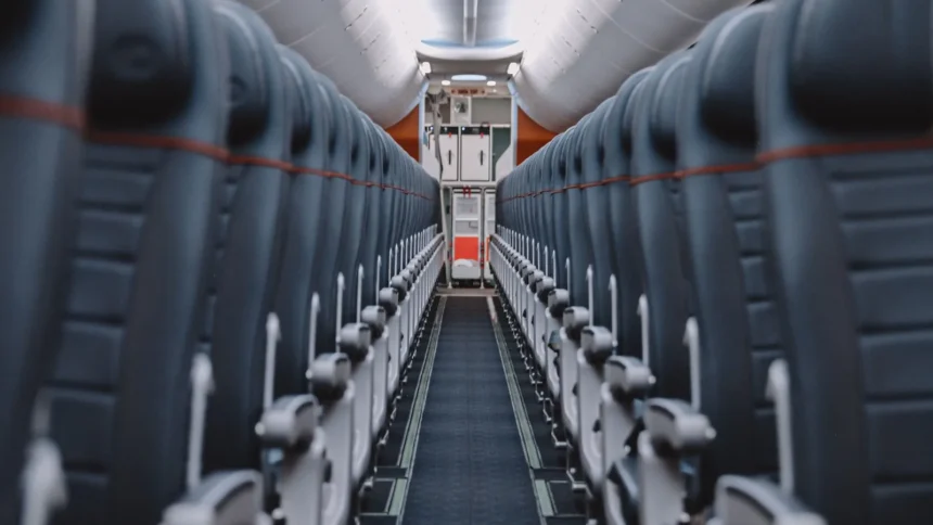 Allée centrale d'une cabine d'avion vide, bordée de rangées de sièges gris dont les appuie-tête portent un liseré orange