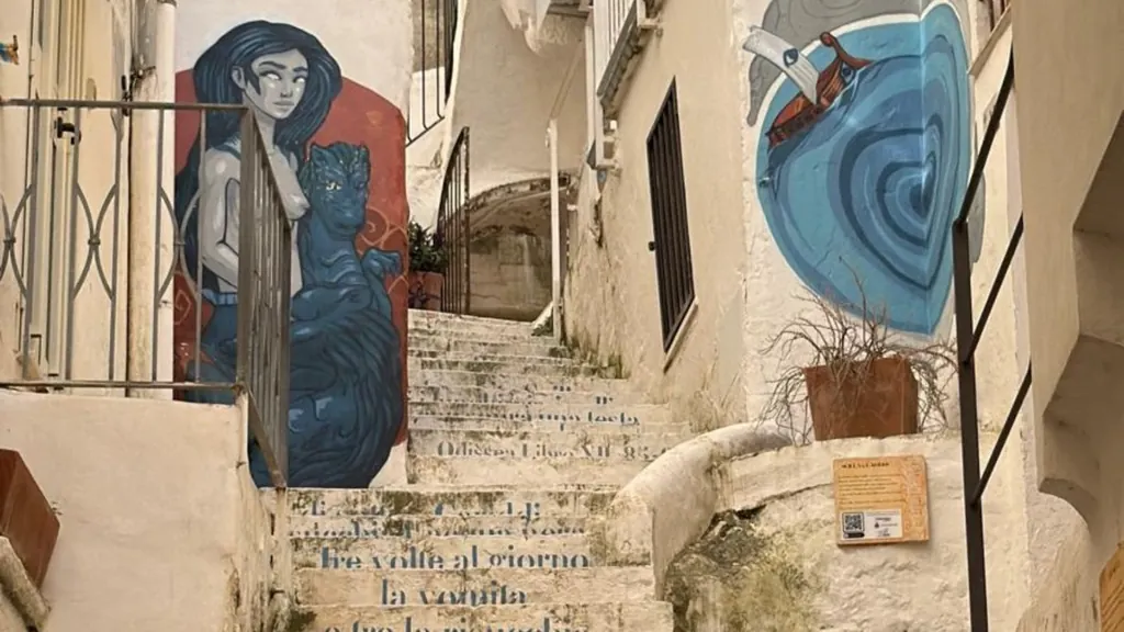 Une journée à Sperlonga depuis Rome : le parcours street art de l'Odyssée 2 Fresque de Scylla et Charybde sur un mur blanc de la via Lebina à Sperlonga, au-dessus d'un escalier portant des vers de l'Odyssée