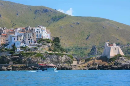 Le village blanc de Sperlonga et la tour Truglia vus depuis la mer, avec un bateau d'excursion au premier plan