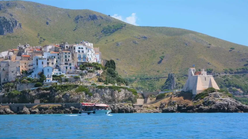Le village blanc de Sperlonga et la tour Truglia vus depuis la mer, avec un bateau d'excursion au premier plan
